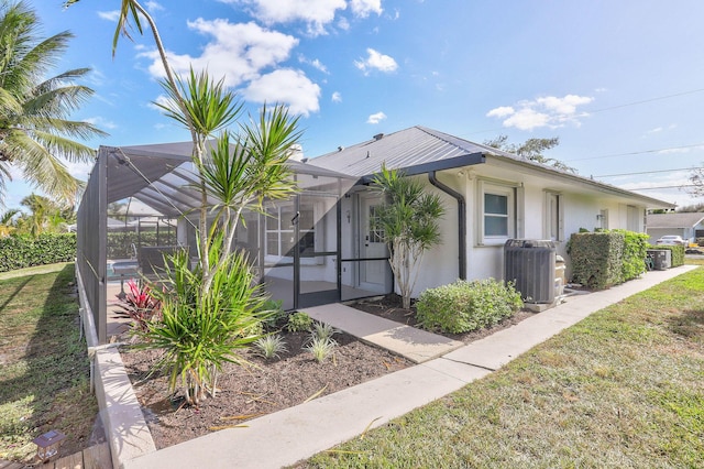 view of front of house with glass enclosure, a front yard, and central AC