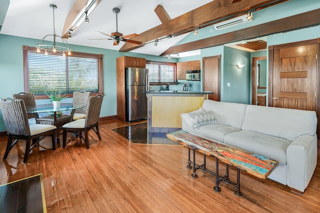 living room with vaulted ceiling with beams, a wealth of natural light, ceiling fan with notable chandelier, and light wood-type flooring