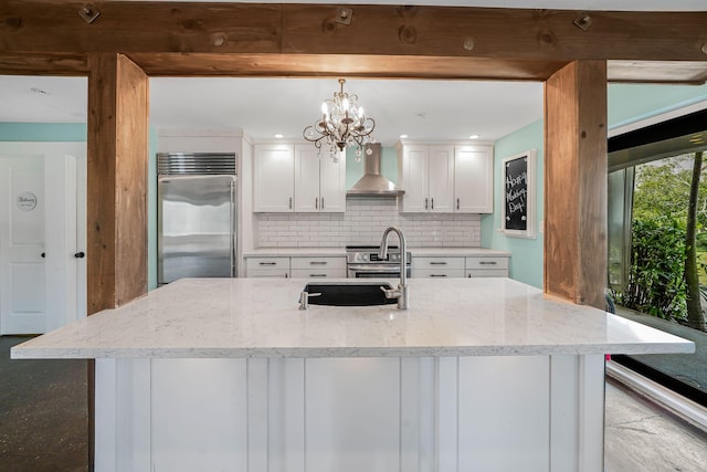 kitchen featuring white cabinets, hanging light fixtures, wall chimney exhaust hood, appliances with stainless steel finishes, and light stone counters