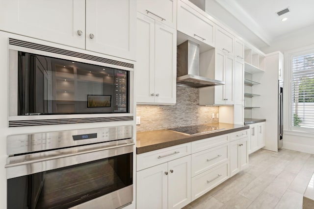 kitchen with white cabinets, wall chimney range hood, decorative backsplash, ornamental molding, and appliances with stainless steel finishes