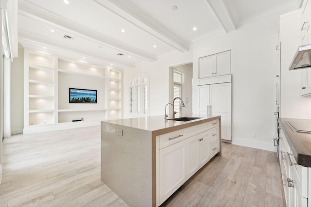 kitchen featuring white cabinets, a kitchen island with sink, beamed ceiling, and light wood-type flooring