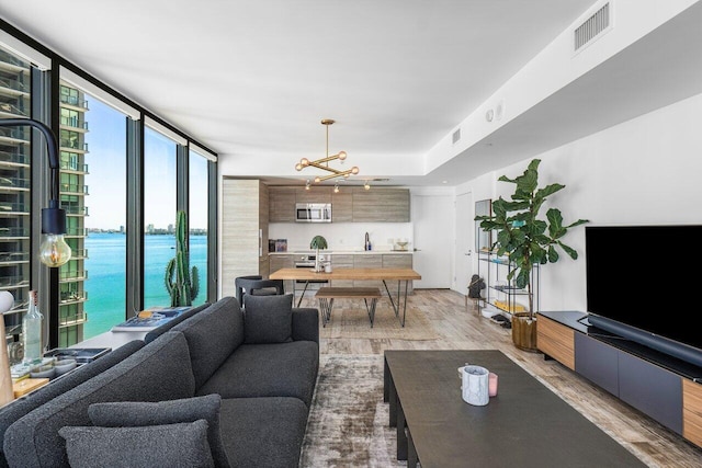 living room featuring hardwood / wood-style flooring, expansive windows, a water view, and a chandelier