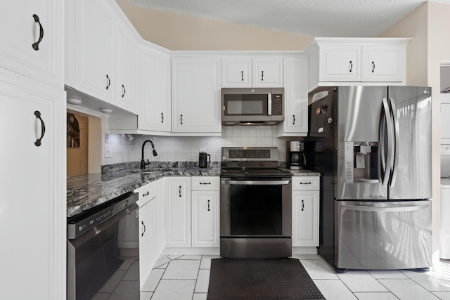 kitchen with sink, dark stone countertops, stainless steel appliances, decorative backsplash, and white cabinets