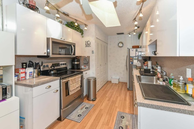 kitchen with white cabinetry, sink, a textured ceiling, appliances with stainless steel finishes, and light wood-type flooring