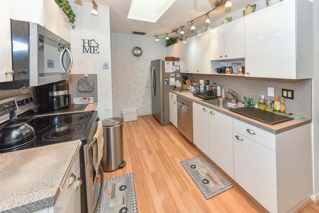 kitchen with a skylight, white cabinets, stainless steel appliances, and a textured ceiling