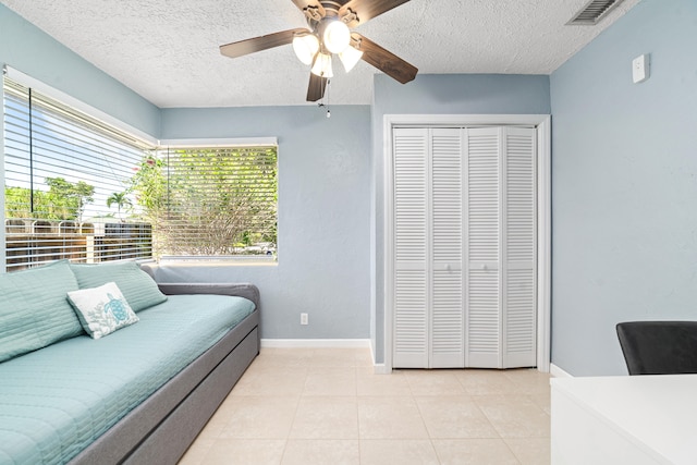 tiled bedroom featuring ceiling fan, a textured ceiling, and a closet