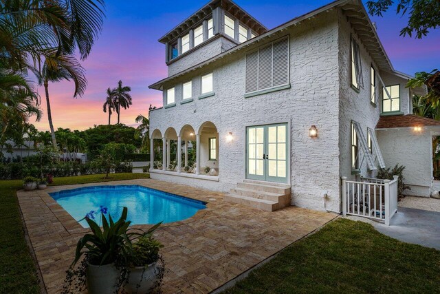 pool at dusk featuring french doors and a patio area