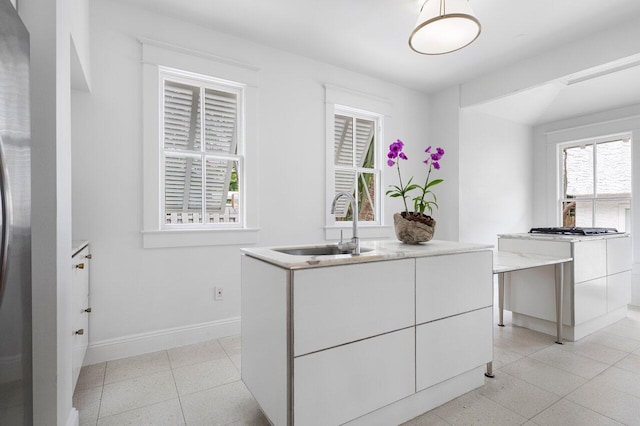 kitchen with white cabinets, light tile patterned floors, a kitchen island, and sink