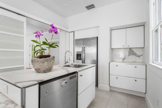 kitchen featuring dishwasher, backsplash, white cabinets, sink, and light stone counters