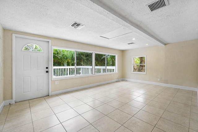 foyer with beamed ceiling, light tile patterned floors, a healthy amount of sunlight, and a textured ceiling