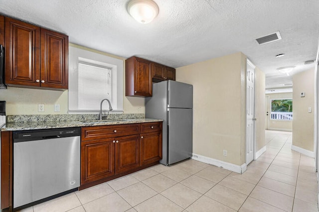 kitchen with light stone countertops, sink, a textured ceiling, light tile patterned flooring, and appliances with stainless steel finishes