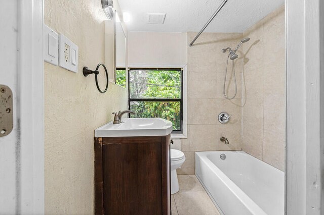 full bathroom featuring vanity, tile patterned floors, tiled shower / bath combo, toilet, and a textured ceiling