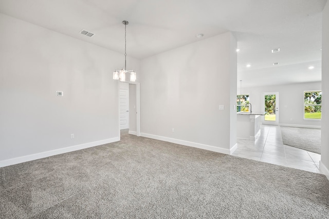 spare room featuring light carpet and an inviting chandelier