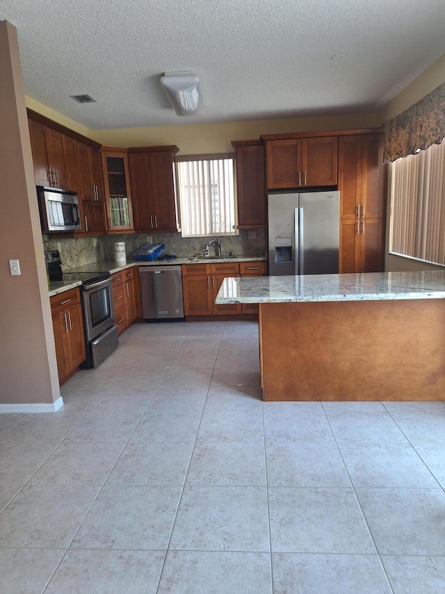 kitchen with backsplash, sink, a textured ceiling, appliances with stainless steel finishes, and light stone counters