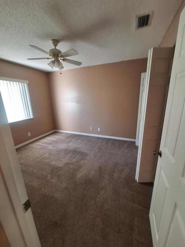 empty room featuring dark colored carpet, a textured ceiling, and ceiling fan