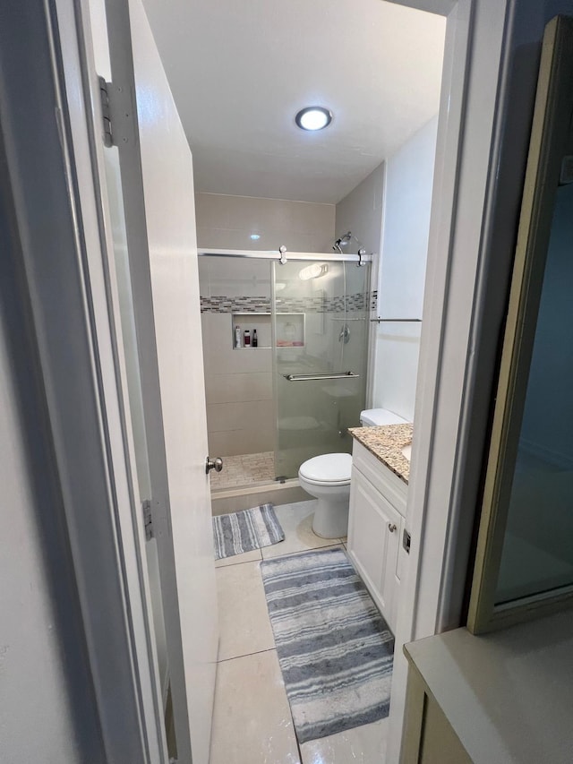 bathroom featuring tile patterned flooring, vanity, toilet, and a shower with shower door