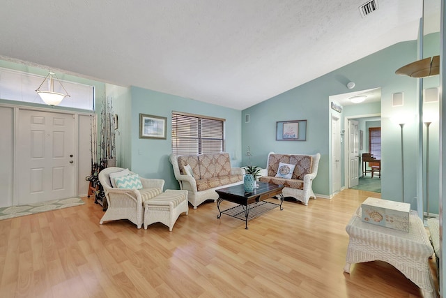 living room with light hardwood / wood-style floors, a textured ceiling, and vaulted ceiling