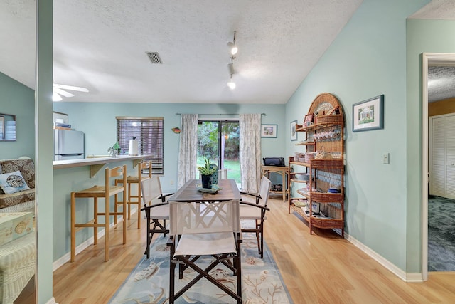 dining space featuring lofted ceiling, ceiling fan, light hardwood / wood-style flooring, and a textured ceiling