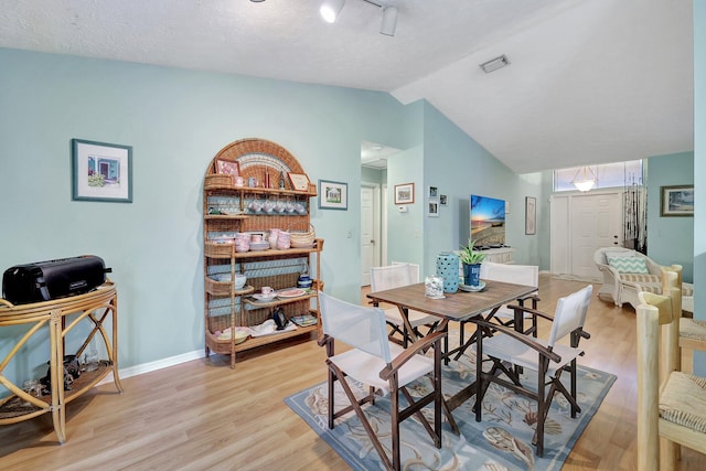 dining space featuring a textured ceiling, light hardwood / wood-style floors, and vaulted ceiling