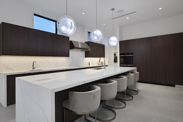 kitchen with backsplash, sink, wall chimney range hood, black oven, and hanging light fixtures