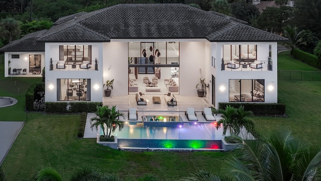 back house at night with an outdoor hangout area, a balcony, a patio area, and a lawn