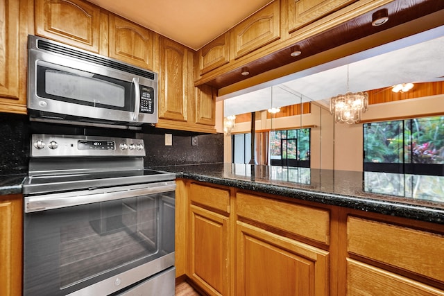 kitchen featuring decorative backsplash, stainless steel appliances, an inviting chandelier, and dark stone countertops