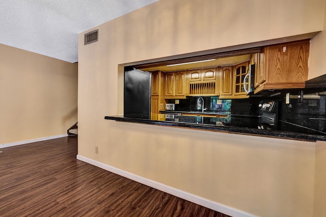 kitchen with sink, dark hardwood / wood-style floors, backsplash, dark stone counters, and a textured ceiling