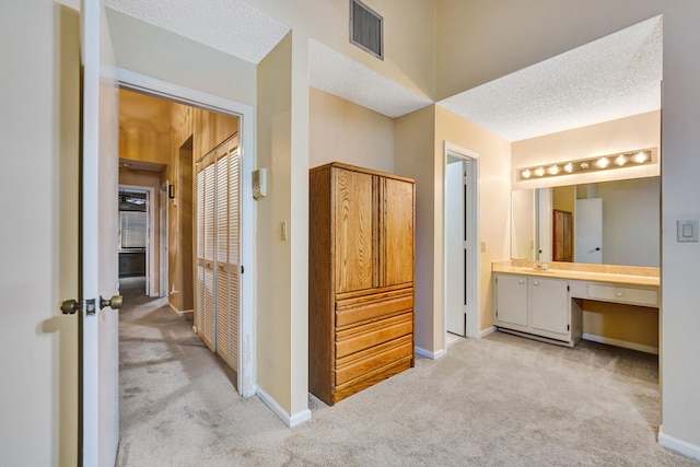 corridor with light colored carpet and a textured ceiling