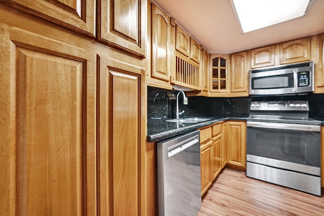 kitchen with sink, dark stone countertops, appliances with stainless steel finishes, tasteful backsplash, and light hardwood / wood-style floors