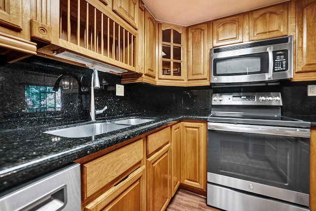 kitchen with backsplash, sink, dark stone countertops, light wood-type flooring, and stainless steel appliances