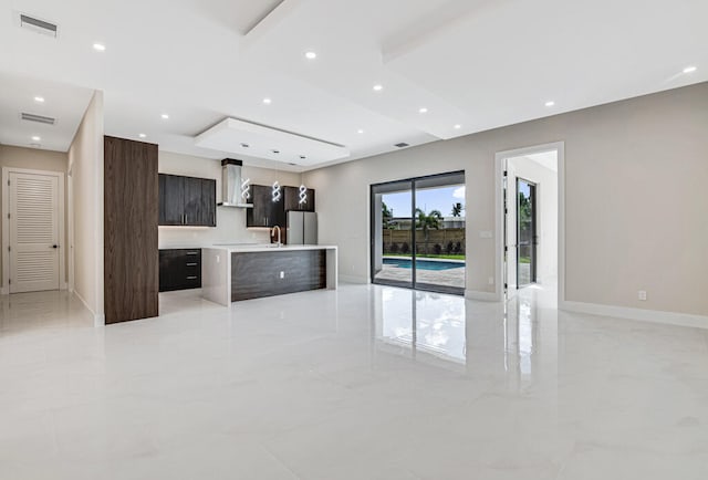 kitchen featuring a center island, wall chimney exhaust hood, decorative light fixtures, dark brown cabinetry, and stainless steel refrigerator