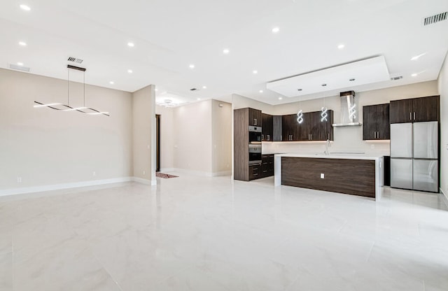 kitchen featuring wall chimney exhaust hood, dark brown cabinets, pendant lighting, a center island, and stainless steel refrigerator