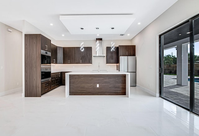 kitchen featuring dark brown cabinetry, wall chimney exhaust hood, hanging light fixtures, a kitchen island with sink, and appliances with stainless steel finishes