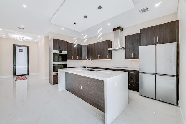 kitchen with sink, hanging light fixtures, wall chimney exhaust hood, double oven, and fridge