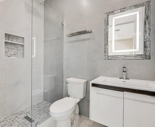 bathroom with tile patterned floors, vanity, tile walls, toilet, and a shower with shower door