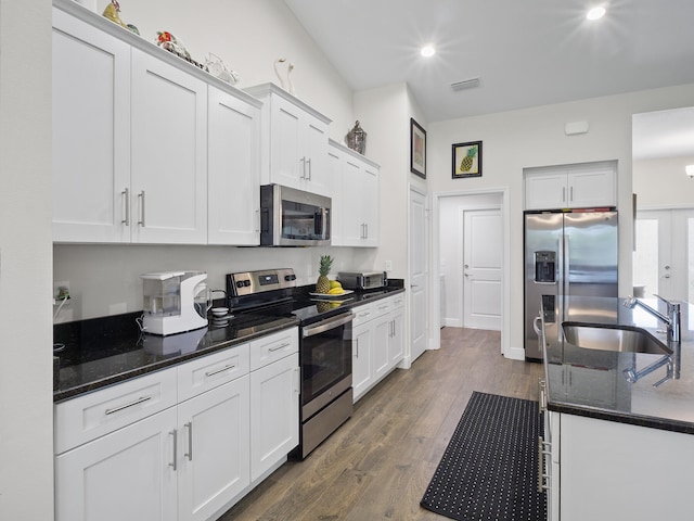 kitchen featuring white cabinetry, sink, stainless steel appliances, dark hardwood / wood-style floors, and dark stone countertops