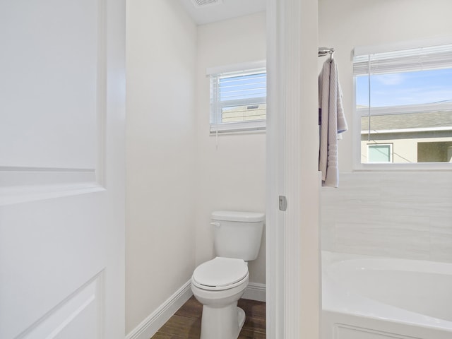 bathroom with a wealth of natural light, a bath, hardwood / wood-style flooring, and toilet