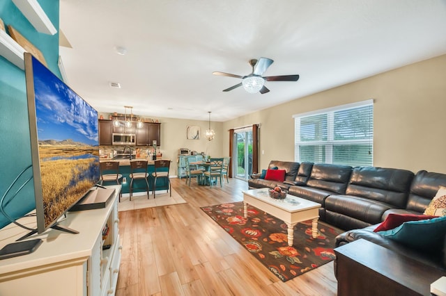 living room featuring ceiling fan with notable chandelier and light wood-type flooring