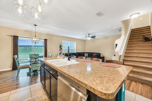 kitchen with sink, stainless steel dishwasher, a kitchen island with sink, ceiling fan with notable chandelier, and light wood-type flooring