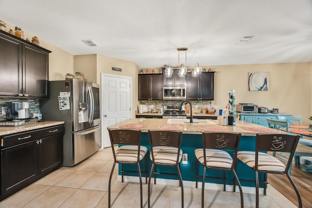 kitchen with pendant lighting, an island with sink, stainless steel appliances, and sink