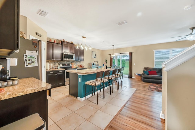 kitchen with a breakfast bar, an island with sink, appliances with stainless steel finishes, dark brown cabinets, and light hardwood / wood-style floors