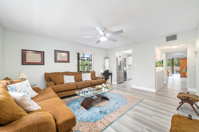 living room with ceiling fan, a textured ceiling, and light hardwood / wood-style flooring