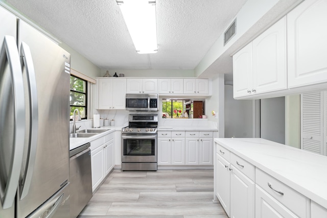 kitchen featuring sink, light wood-type flooring, a textured ceiling, appliances with stainless steel finishes, and white cabinetry