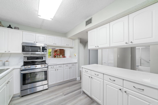 kitchen featuring white cabinets, a textured ceiling, stainless steel appliances, and light hardwood / wood-style flooring