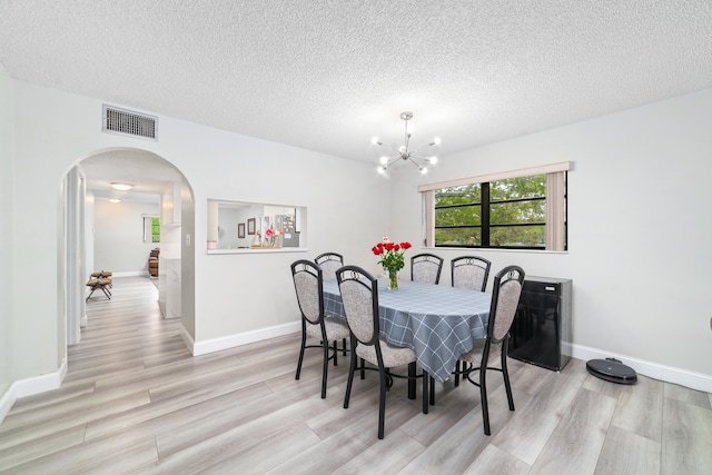 dining space with light hardwood / wood-style flooring, a textured ceiling, and an inviting chandelier