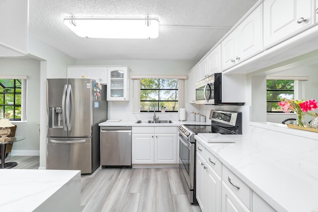 7579 NW 79th Ave Unit 201, Tamarac, FL 33321 - kitchen featuring a textured ceiling, appliances with stainless steel finishes, light stone countertops, a sink, and white cabinets