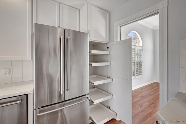 kitchen with white cabinets, stainless steel appliances, light hardwood / wood-style floors, backsplash, and light stone counters