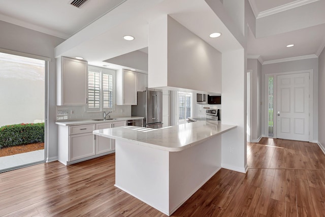 kitchen featuring white cabinetry, kitchen peninsula, appliances with stainless steel finishes, crown molding, and sink