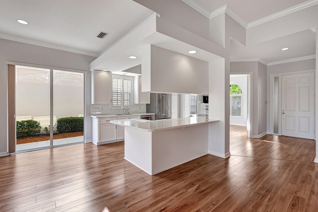 kitchen featuring kitchen peninsula, high end refrigerator, white cabinets, crown molding, and light hardwood / wood-style flooring