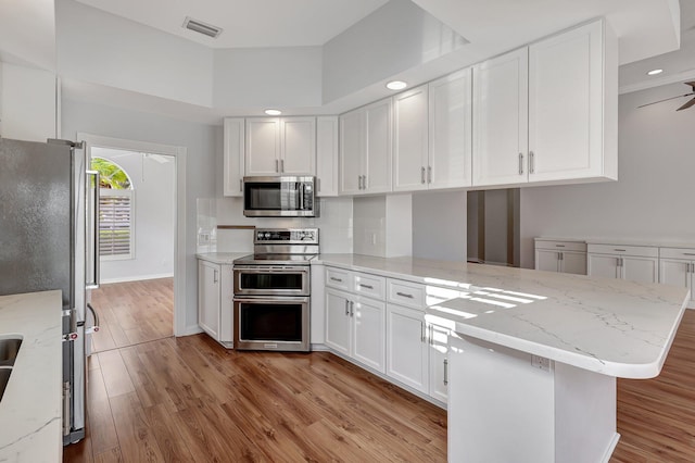 kitchen featuring white cabinetry, kitchen peninsula, ceiling fan, appliances with stainless steel finishes, and light wood-type flooring